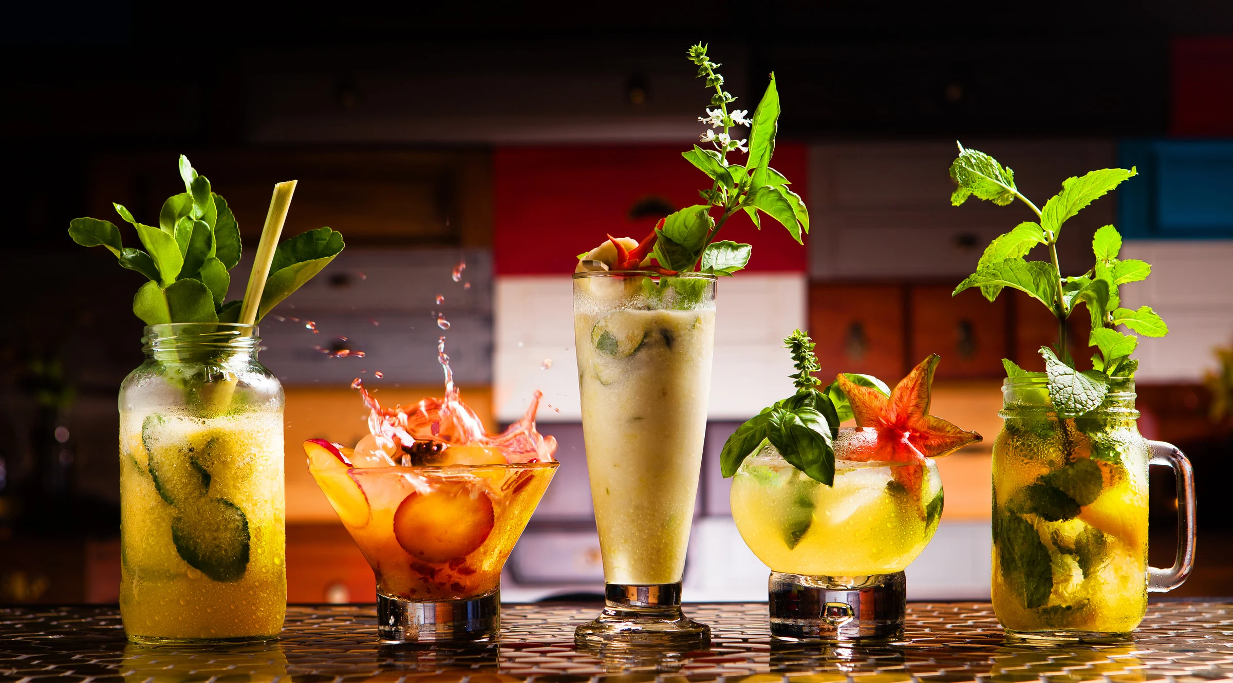 Five styled cocktails with fresh herbs and fruit in a bar setting